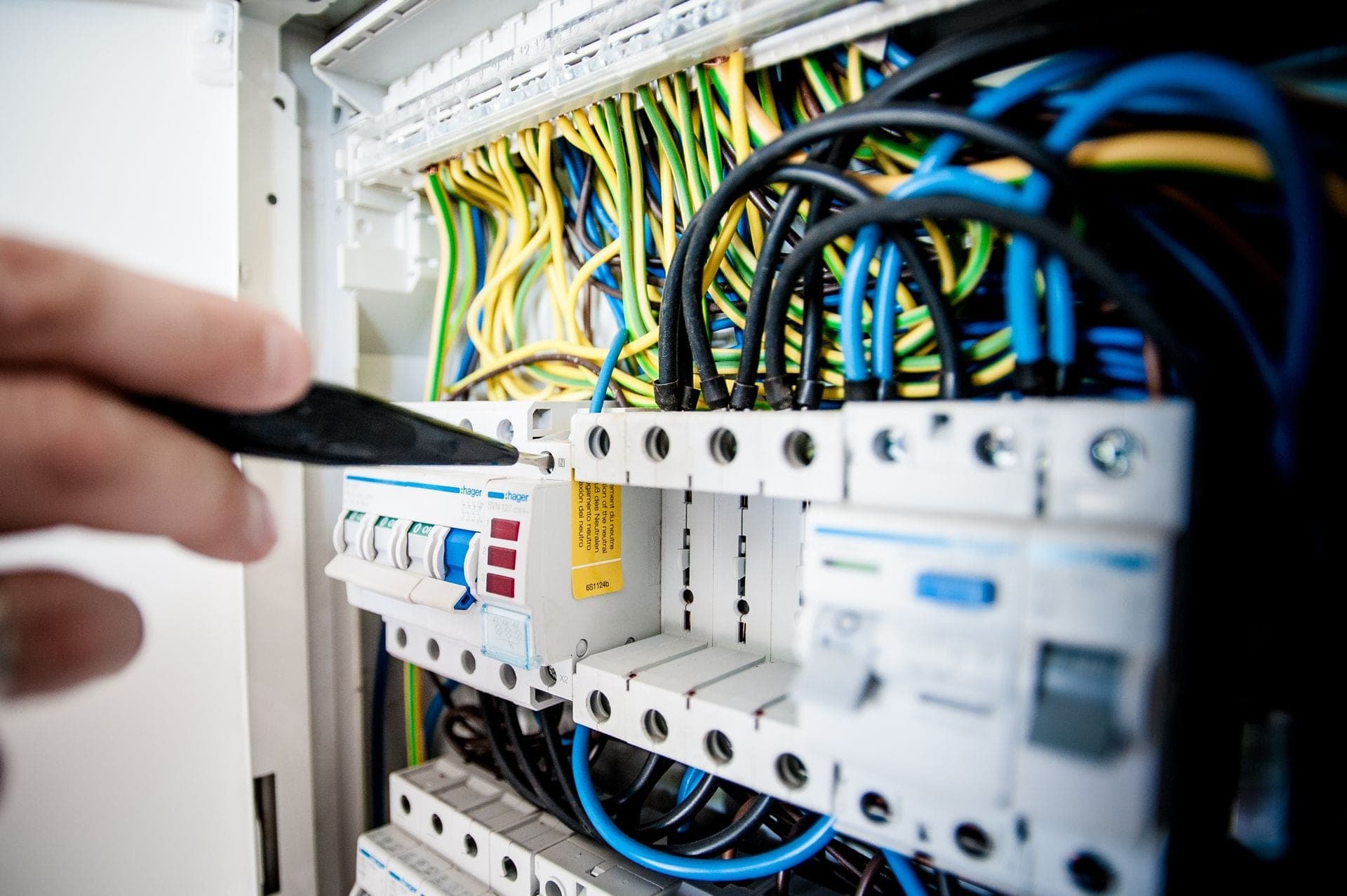 A hand testing connections on an electrical breaker panel.